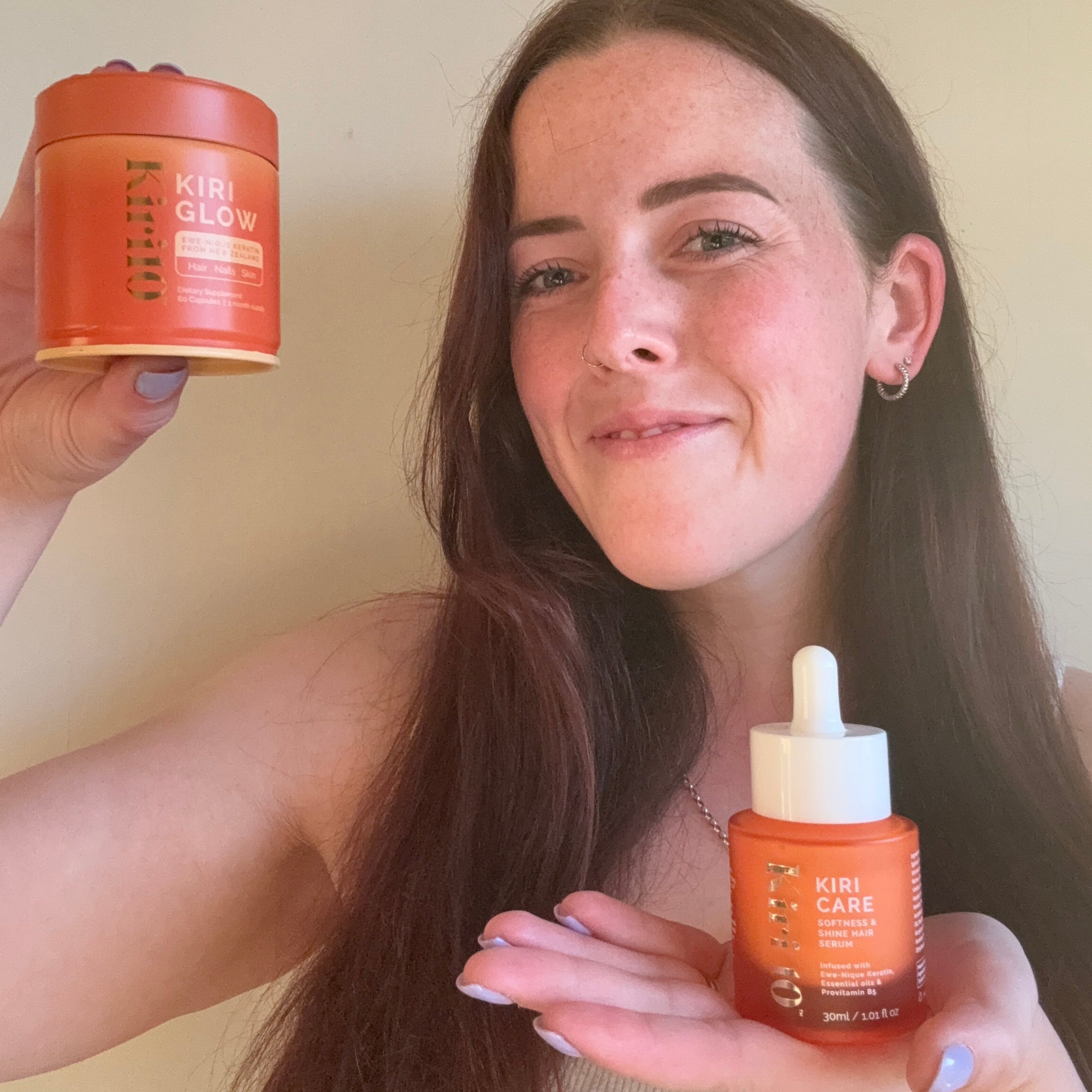 Woman holding two bottles of Kiri10 hair care products against a neutral background